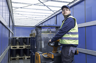 A Leadec employee with safety vest loading a coil pallet from a truck with an electric pallet truck.