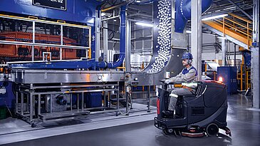 Leadec employee driving cleaning machine on shopfloor of Food & Beverage factory.